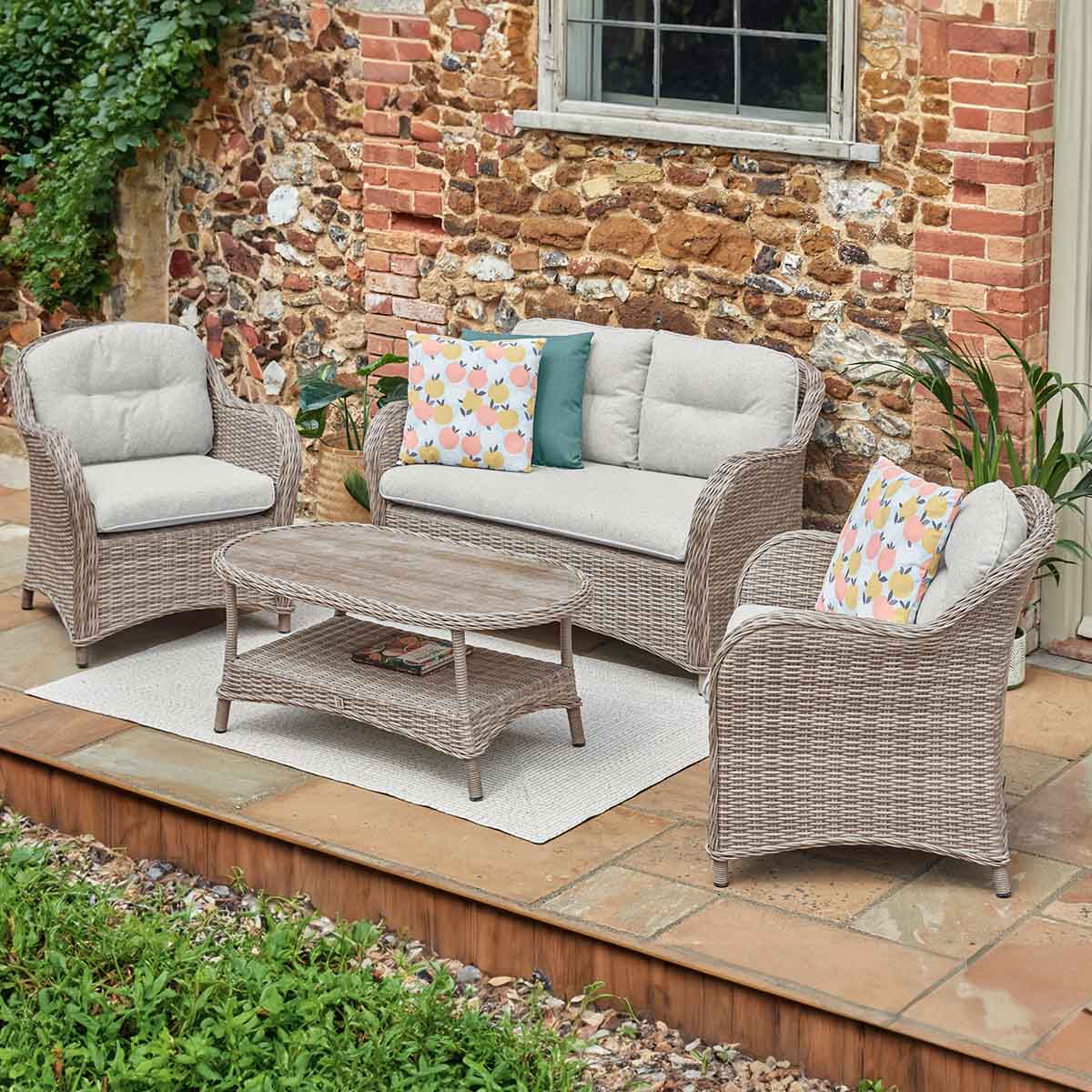 St Tropez Sand Outdoor patio set with wicker furniture on a stone patio against a brick wall.