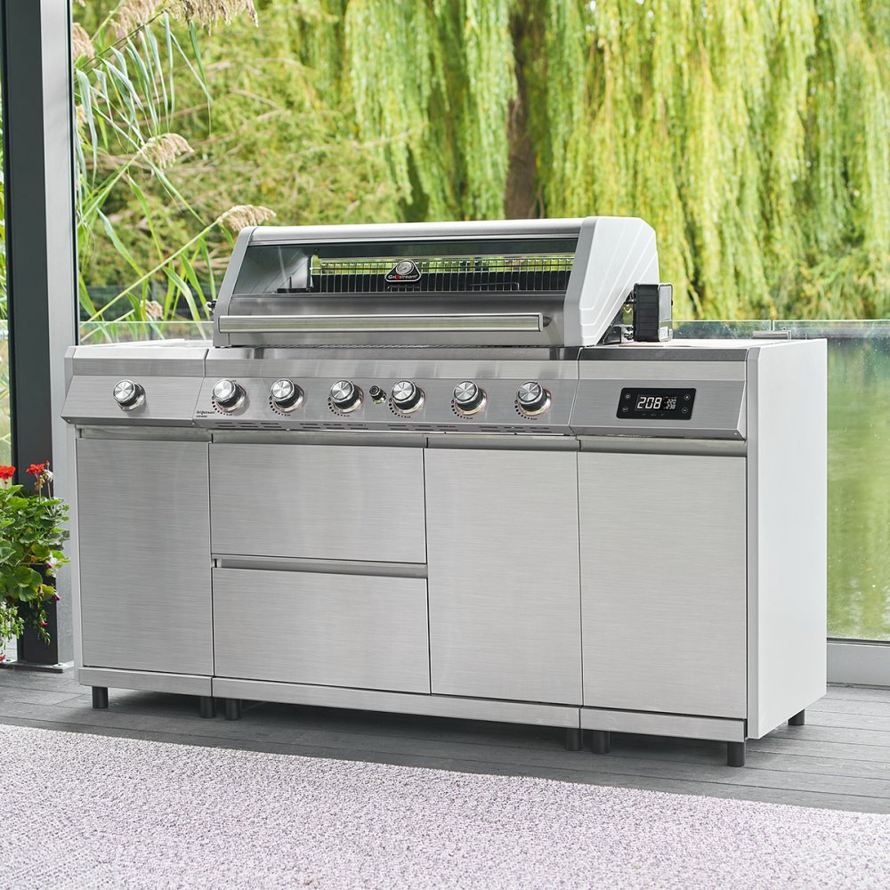 A stainless steel Grillstream Island 6 Burner Hybrid Gas & Charcoal BBQ with six main burners, side shelves and a closed hood, set against an outdoor backdrop.